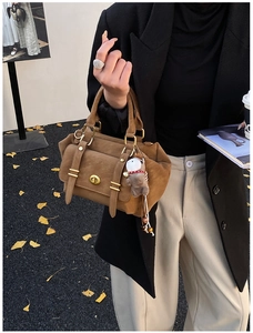 Detail of retro brown handbag with gold turn-lock and plush charm in autumn street style