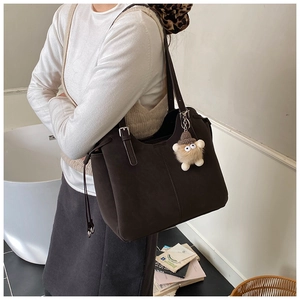 Detail of dark brown matte leather tote bag with a cute plush charm and long strap