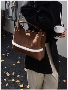 Detail of brown suede tote bag with white plush trim and golden chain strap on autumn street