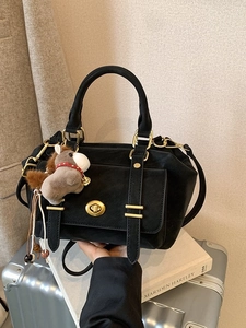 Retro black leather handbag with gold hardware and horse charm on grey luggage