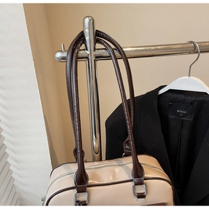 Detail of beige shoulder bag with dark brown handles and polished silver hardware