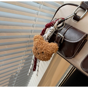 Brown teddy plush bear keychain with woven rope detail on a brown leather shoulder bag