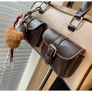Detail of retro color-block tote bag featuring dual front pockets and brown plush bear charm