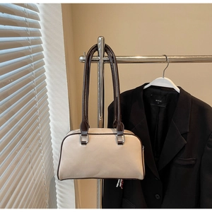 Close-up of cream shoulder bag with dark brown handles and silver metal hardware detail
