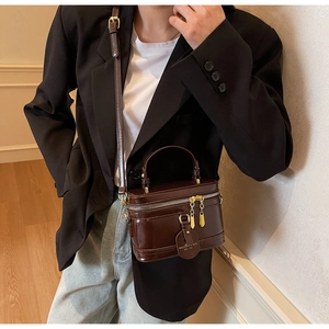 Model trägt eine dunkelbraune Retro-Box-Tasche mit Glanzeffekt und goldenem Anhänger