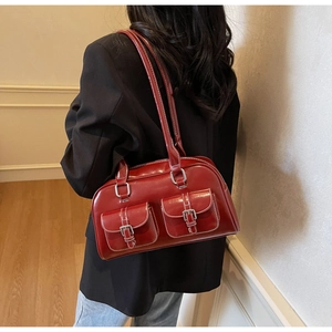 Detail of burgundy glossy leather shoulder bag with double pockets worn by a model
