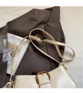 Detail of cream shoulder bag featuring adjustable strap and large metal buckle detail