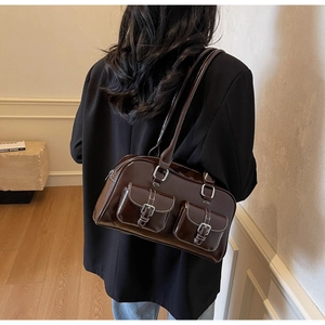 Detail of dark brown patent leather tote with contrast stitching and silver buckle pockets