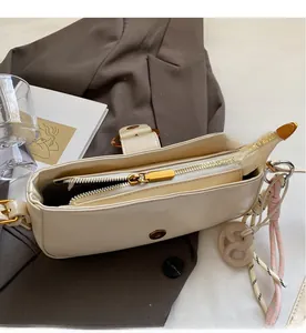 Detail view of beige leather shoulder bag showing smooth golden zipper and woven charm