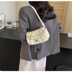 Close-up of beige ruched cloud bag with silver heart chain and woven strap detail