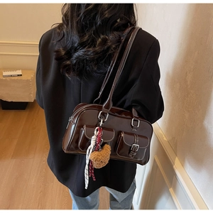 Detail of dark brown patent leather shoulder bag with white stitching and plush bear charm