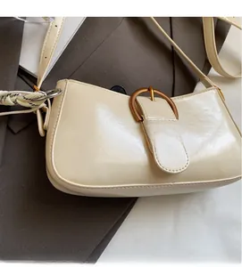 Detail of cream white faux leather underarm bag with gold buckle and silk scarf accent