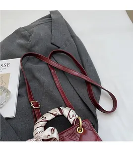 Detail of burgundy quilted handbag with floral silk scarf wrap on handle and gold hardware