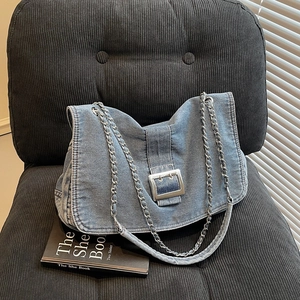 Sac à bandoulière en denim bleu avec chaîne argentée et boucle sur une chaise noire