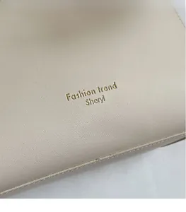 Detail of the golden Sheryl logo on minimalist beige litchi textured leather tote bag