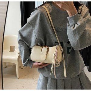 Detail of cream white faux leather bag featuring a vintage metal buckle and braided charm