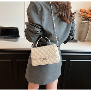Detail of beige quilted flap bag featuring metal chain strap and top handle in a minimalist setting
