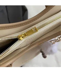 Close-up of golden zipper puller and fine stitching on a beige leather shoulder bag