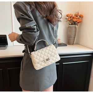 Close-up of quilted cream shoulder bag featuring metal turn-lock and chain strap detail