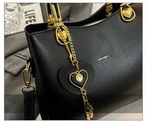 Detailed close-up of heart-shaped gold pendant and crystal charm on black leather handbag