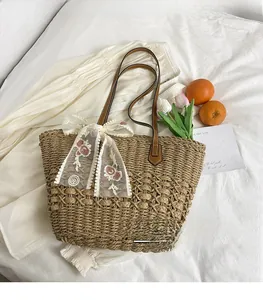 Detail of woven straw tote bag with lace floral embroidery and brown leather handles