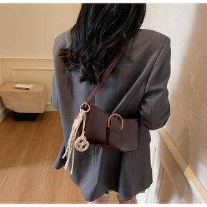 Detail view of dark brown leather underarm bag with metal buckle and woven knot charm