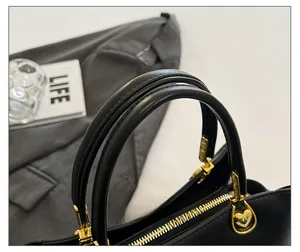 Detail of round leather handles and golden heart-shaped hardware on a black handbag