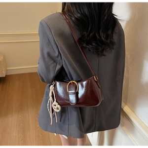 Detail of burgundy patent leather underarm bag with gold buckle and woven charm