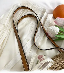 Detail of dark brown leather strap with white stitching on a woven straw bag