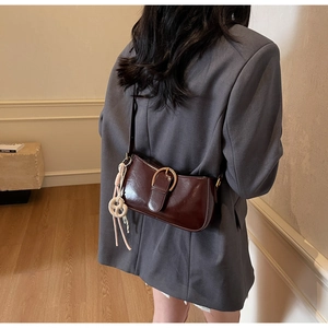 Detail of a dark burgundy glossy shoulder bag with a large gold buckle and white charm