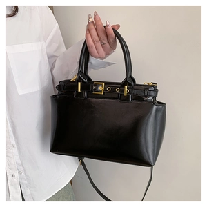 Détail du sac cabas noir brillant avec boucle dorée et bandoulière longue amovible
