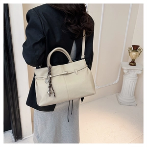 Détail du sac cabas en cuir grainé beige avec pendentif métallique et pompon chic