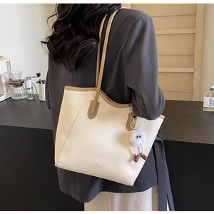 Detail of cream leather tote bag with brown trim and plush charm worn on shoulder