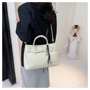 Détail du grand sac cabas en cuir crème avec breloque métallique et bandoulière tressée