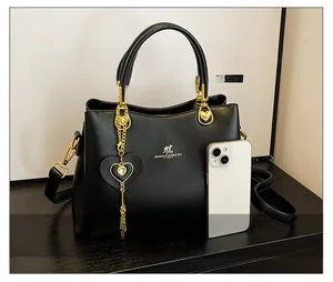 Detail of black structured handbag with gold kangaroo logo and heart-shaped gemstone charm