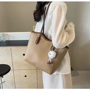 Detail view of large khaki tote bag with plush ball charm and Fashion Trend gold lettering