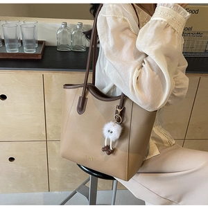 Detail of a color-block tote bag in khaki and coffee brown with a fluffy white pendant