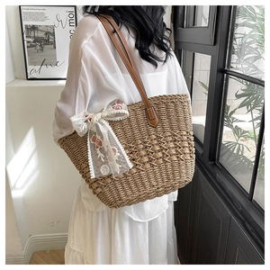 Detail of woven straw tote bag with brown leather handles and lace bow accent