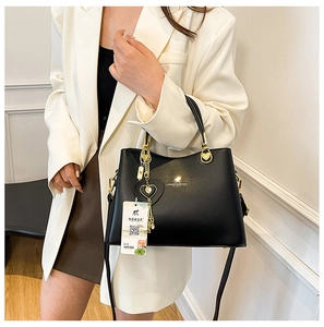 Detail of black pebbled leather handbag with gold kangaroo logo and tassel charm on model