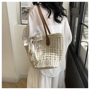 Detail of woven straw tote bag featuring white lace bow with delicate floral embroidery