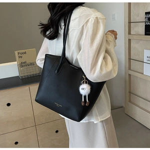 Detail of black textured PU leather tote bag with a white fluffy ball charm accessory