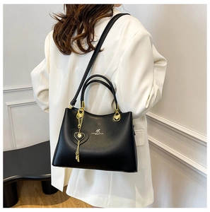 Detail of black matte leather handbag featuring a golden kangaroo logo and heart charm