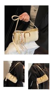 Close-up of a cream underarm bag with a round buckle and woven rope decorative pendant