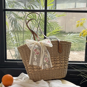 Woven straw tote bag with brown leather handles and a floral embroidered lace bow