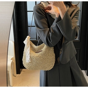 Close-up of woven straw bucket bag featuring a brown leather strap and white lace ribbon