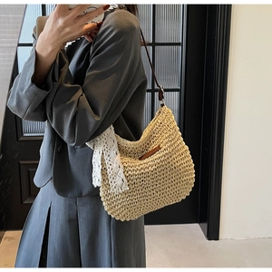 Detail of hand-woven straw crossbody bag with white lace bow and brown leather strap