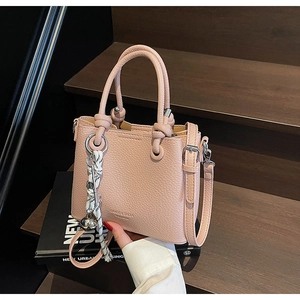 Pink lychee grain leather mini bag with striped knot charm on dark wood steps
