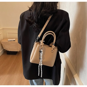 Detailed close-up of a light brown litchi pattern leather tote with striped ribbon charm