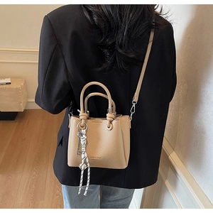 Detail of beige lychee grain leather bag with knot handles and decorative bag charm