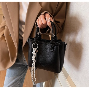 Detail of black lychee leather handbag featuring woven charm and silver hardware